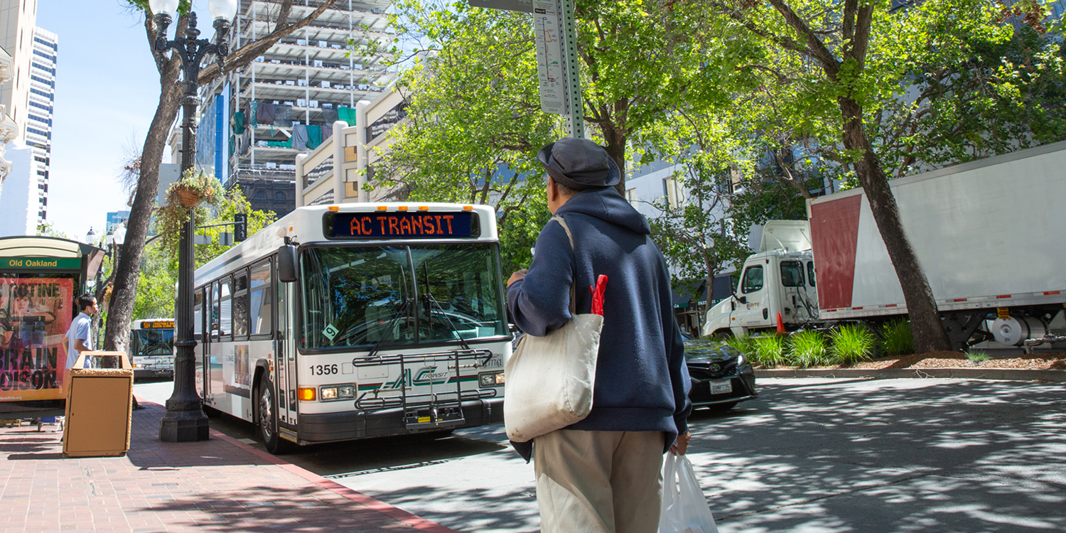 AC Transit bus approaching stop, with pedestrian onlooking